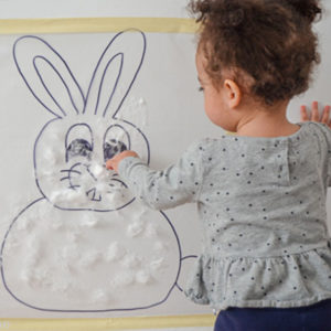 lavoretti di pasqua metodo Montessori, bambina attacca batuffoli di cotone al coniglietto di carta
